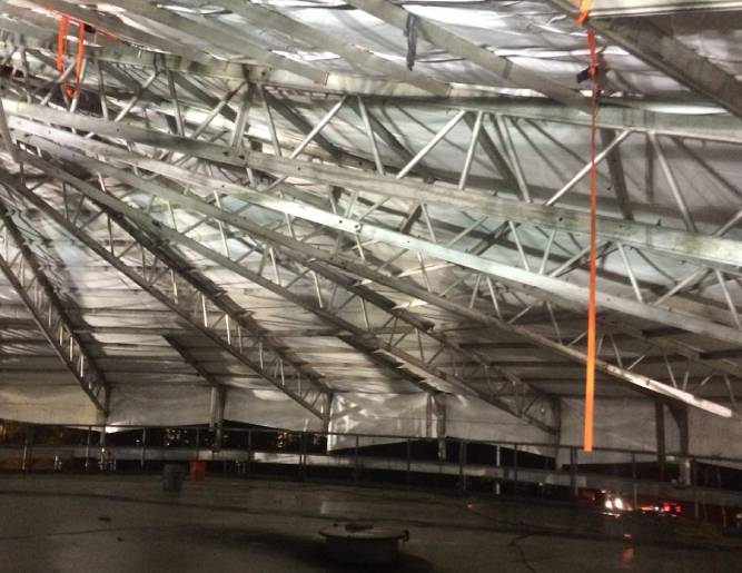 Premier Scaffold Inc. is covering the roof of a metal structure with tarps.